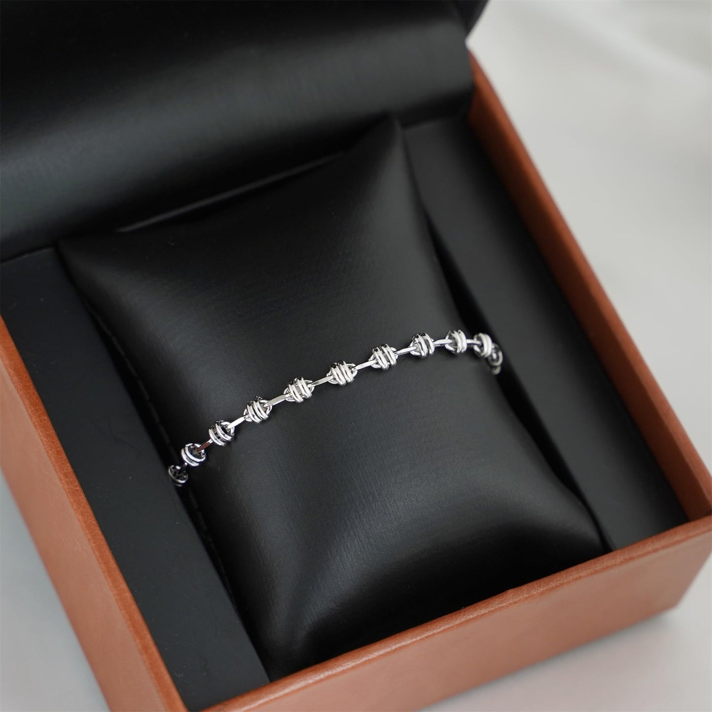 Silver-tone oval curb bracelet resting in a gift box with link detail