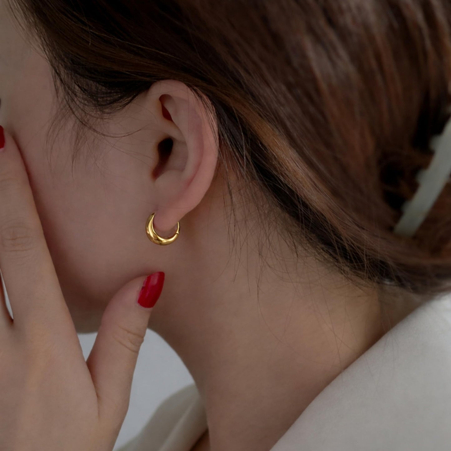 Gold teardrop hoop huggie earring on ear, glossy curved shape with open slot.
