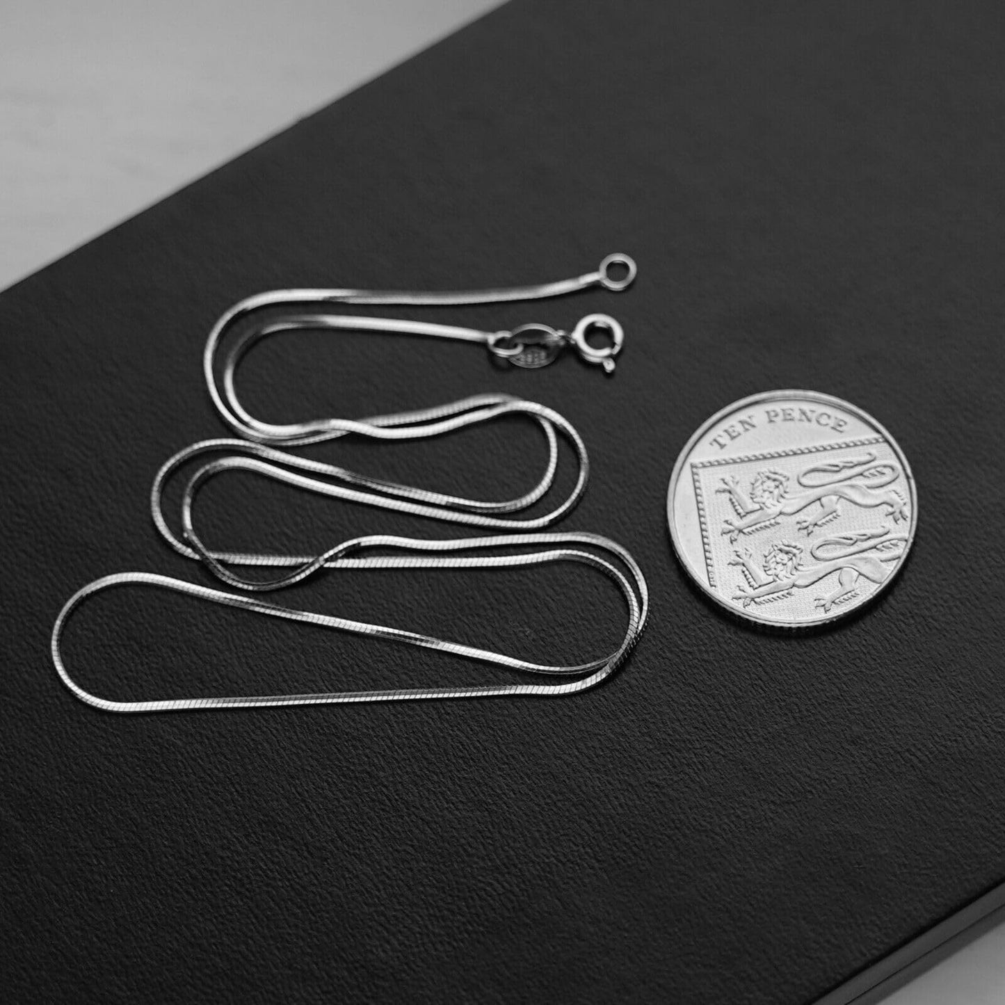 Silver snake chain necklace lengths with clasps and hooks, laid flat with coin