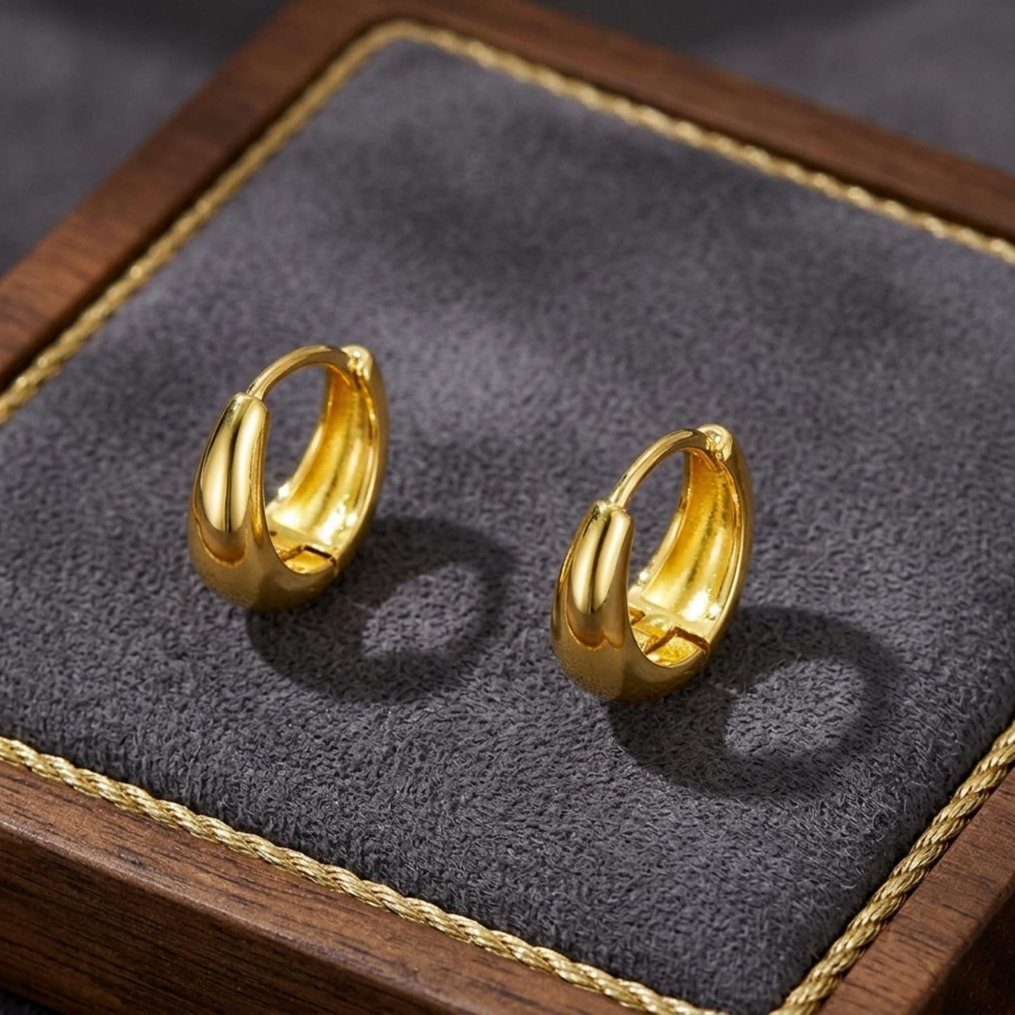 Gold teardrop hoop huggie earrings with glossy finish, shown as a pair on tray.