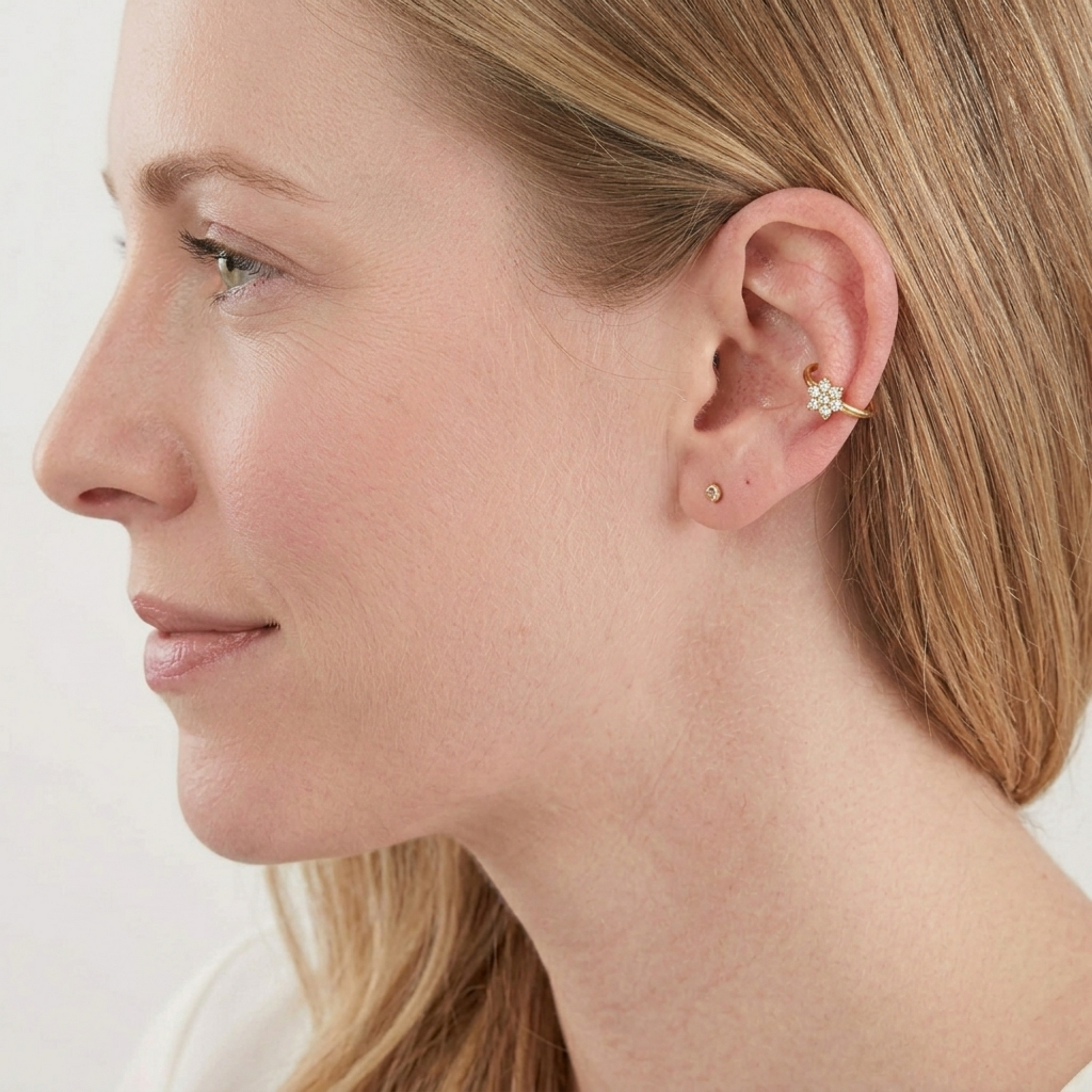Silver CZ floral cuff hoop earring on ear, with a small flower cluster.