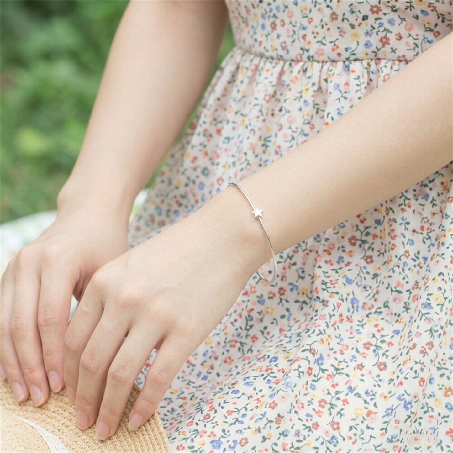 Silver star charm bangle on wrist, worn with a floral dress