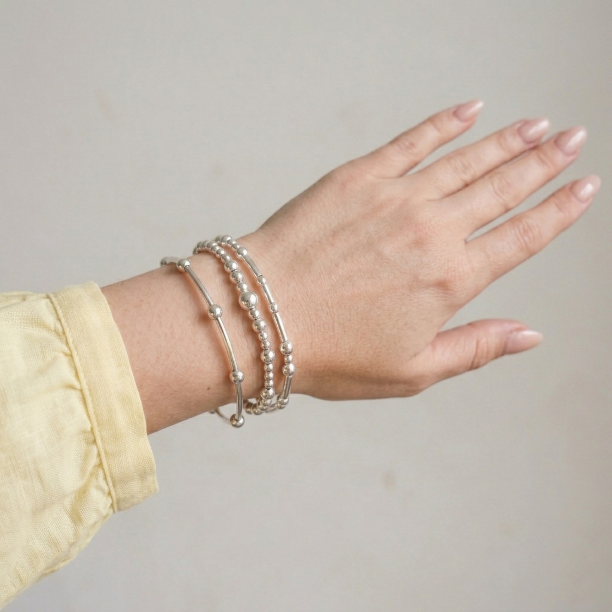 Stacked silver stretch bracelets with round beads on a wrist