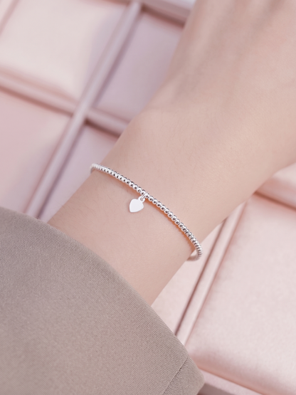 Silver beaded stretch bracelet with heart charm and smooth curved bar on wrist