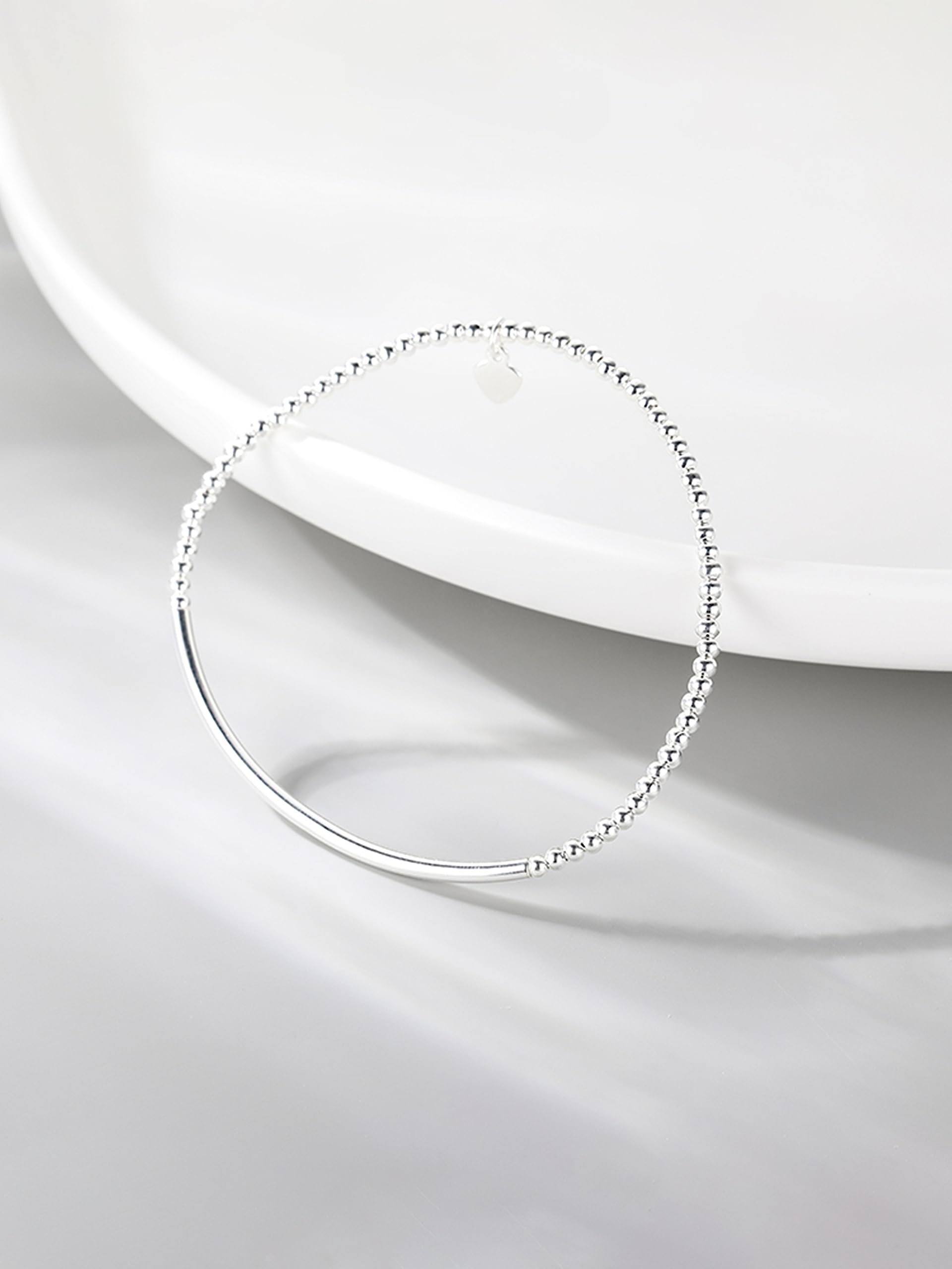 Silver beaded stretch bracelet with heart charm and smooth curved bar on white dish