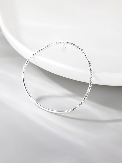 Silver beaded stretch bracelet with heart charm and smooth curved bar on white dish