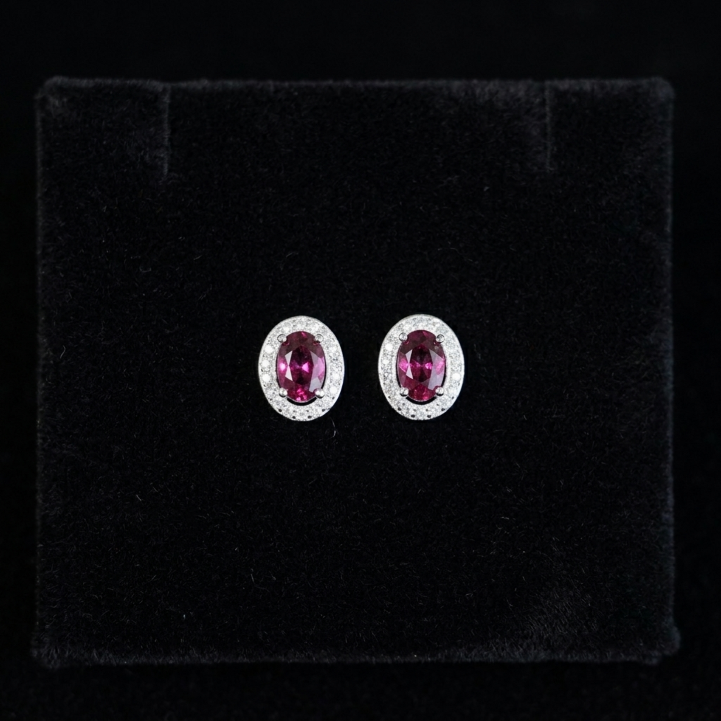 Oval ruby-red CZ stud earrings with silver halo and small round stones