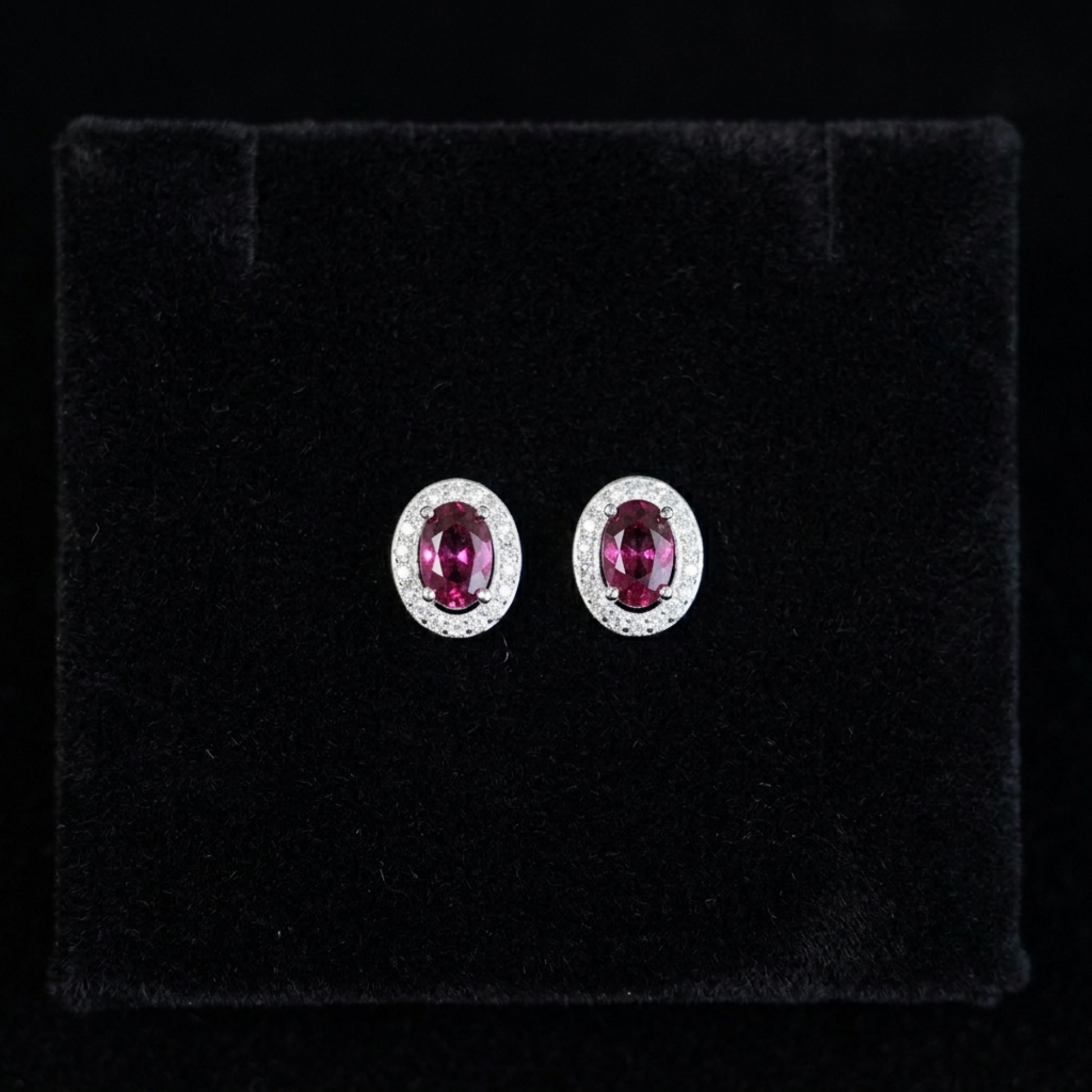Oval ruby-red CZ stud earrings with silver halo and small round stones