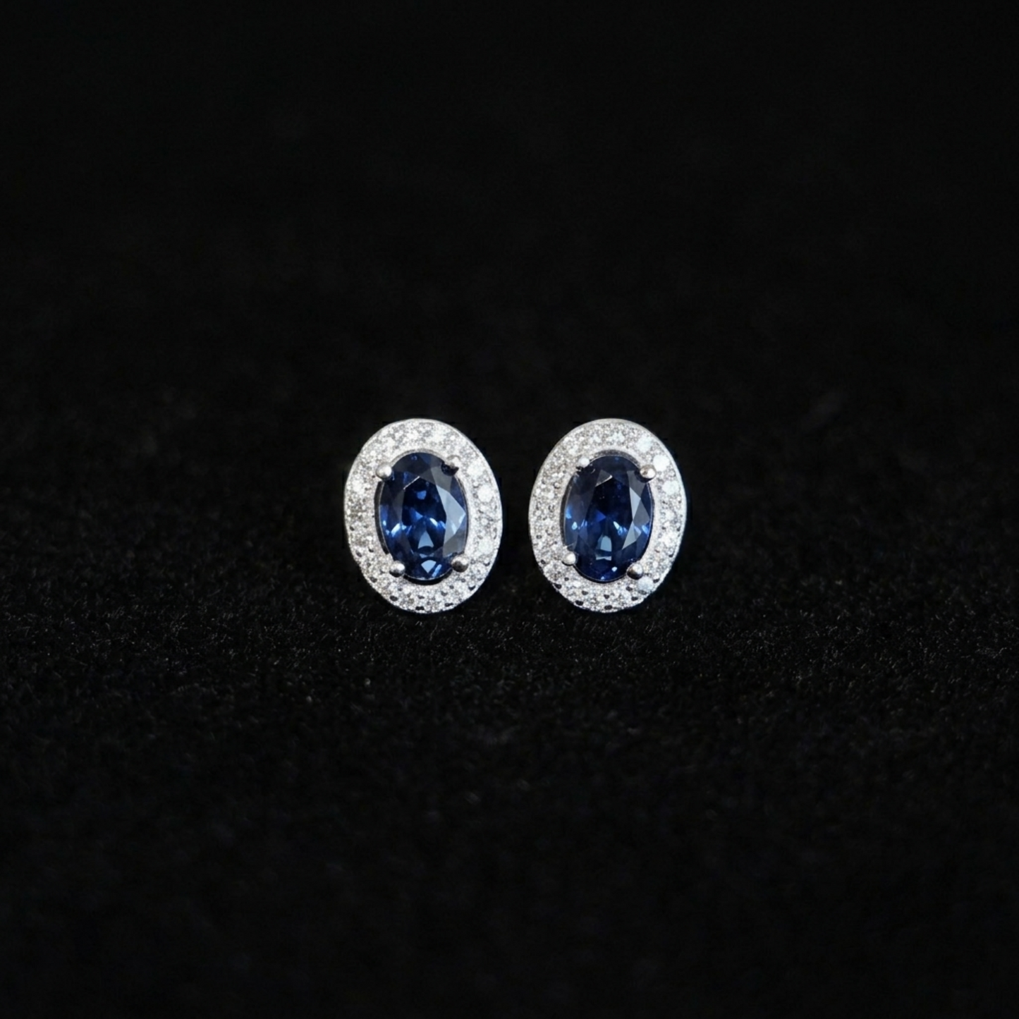 Oval halo CZ stud earrings with deep blue oval stones in silver pavé halo