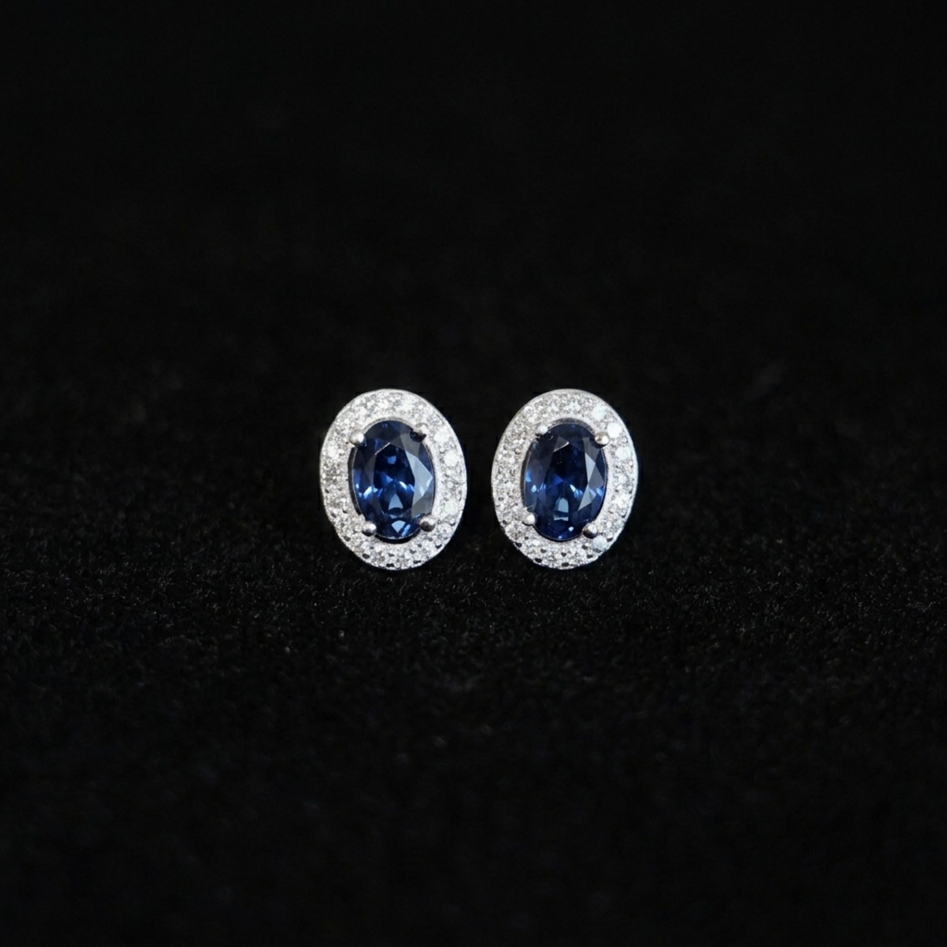 Oval halo CZ stud earrings with deep blue oval stones in silver pavé halo