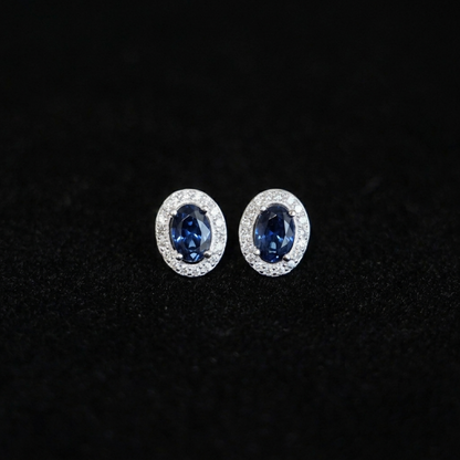 Oval halo CZ stud earrings with deep blue oval stones in silver pavé halo