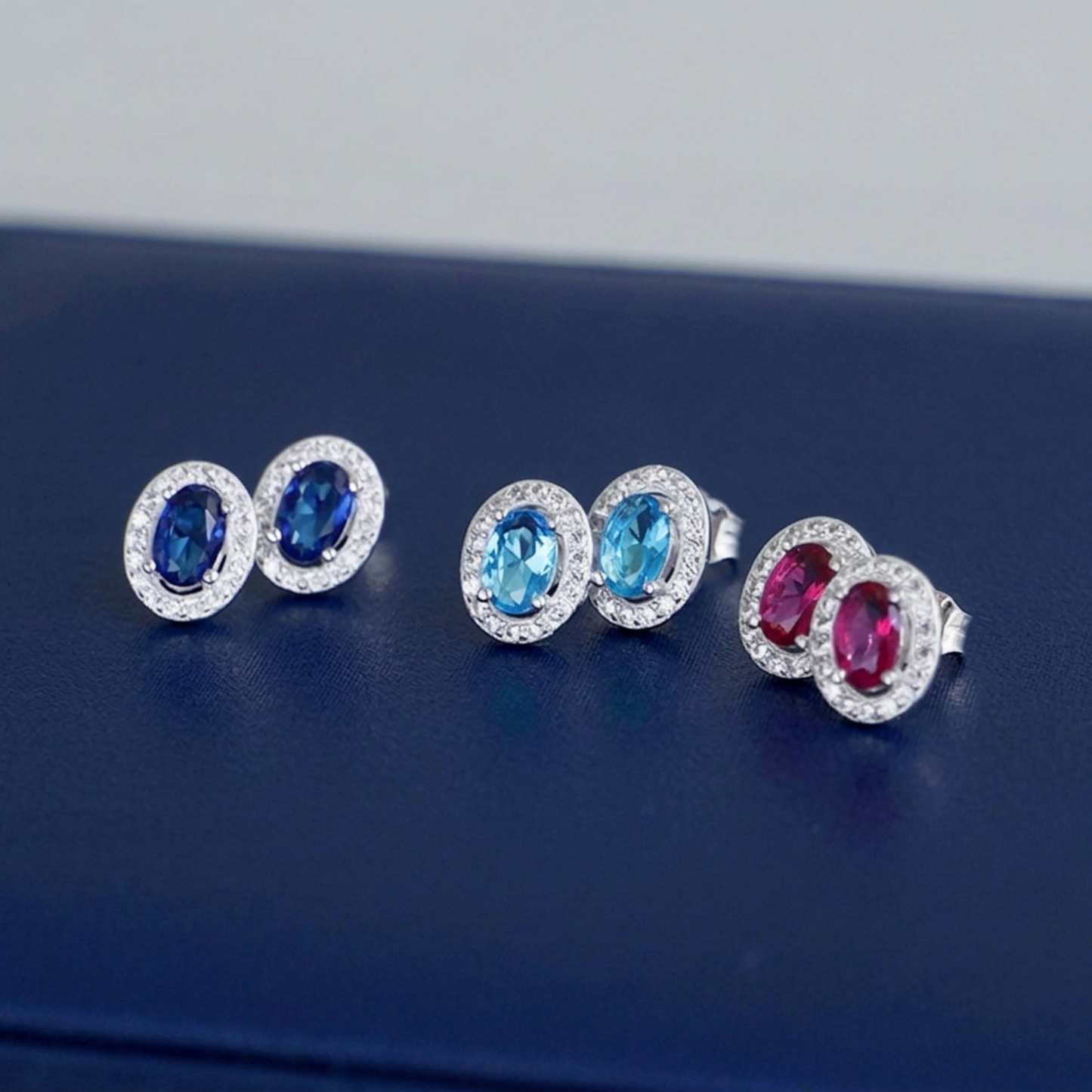 Halo CZ stud earrings with dark blue and pink/red oval stones, silver-toned settings
