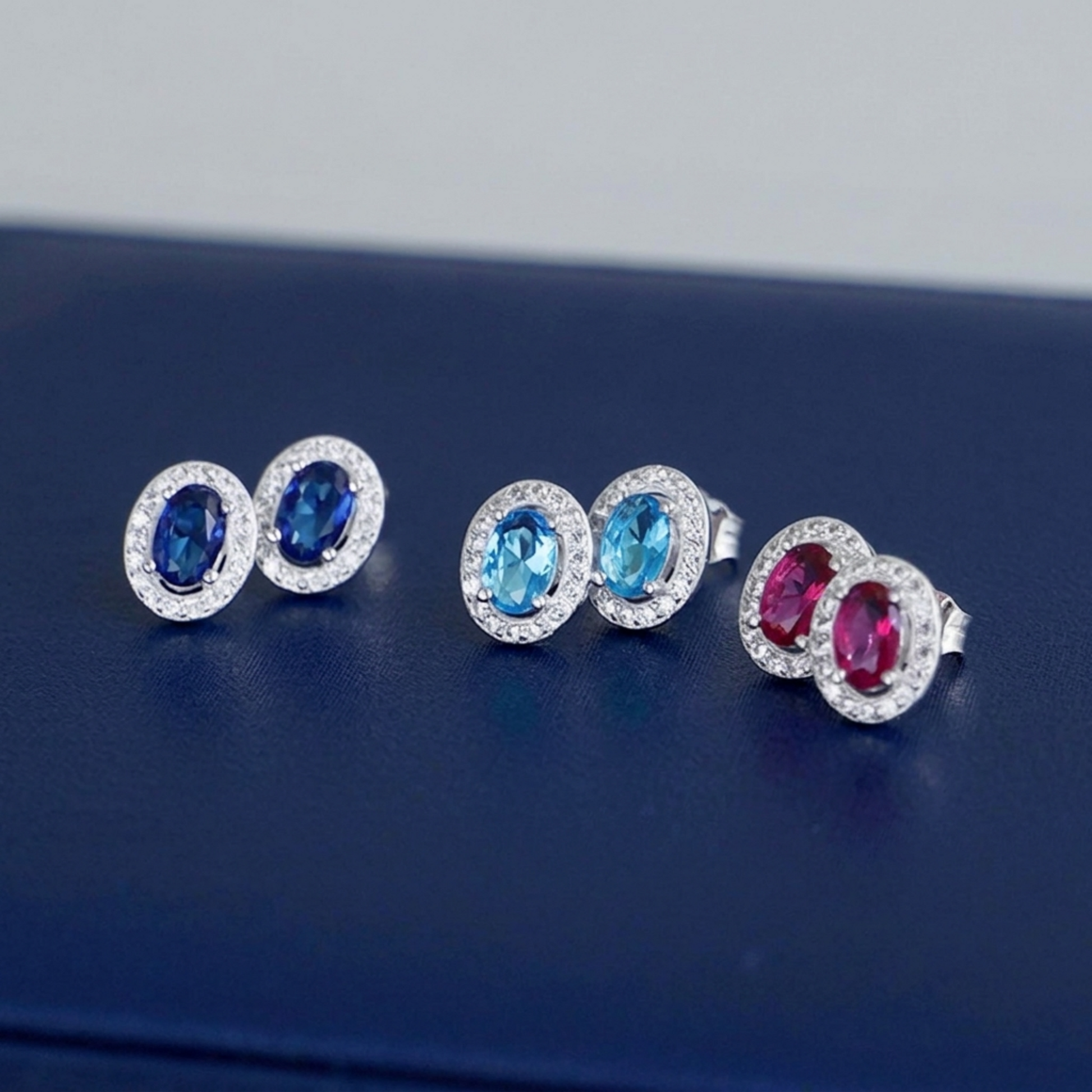 Halo CZ stud earrings with dark blue and pink/red oval stones, silver-toned settings