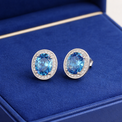 Blue gemstone stud earrings with circular CZ halo edging and silver-tone posts