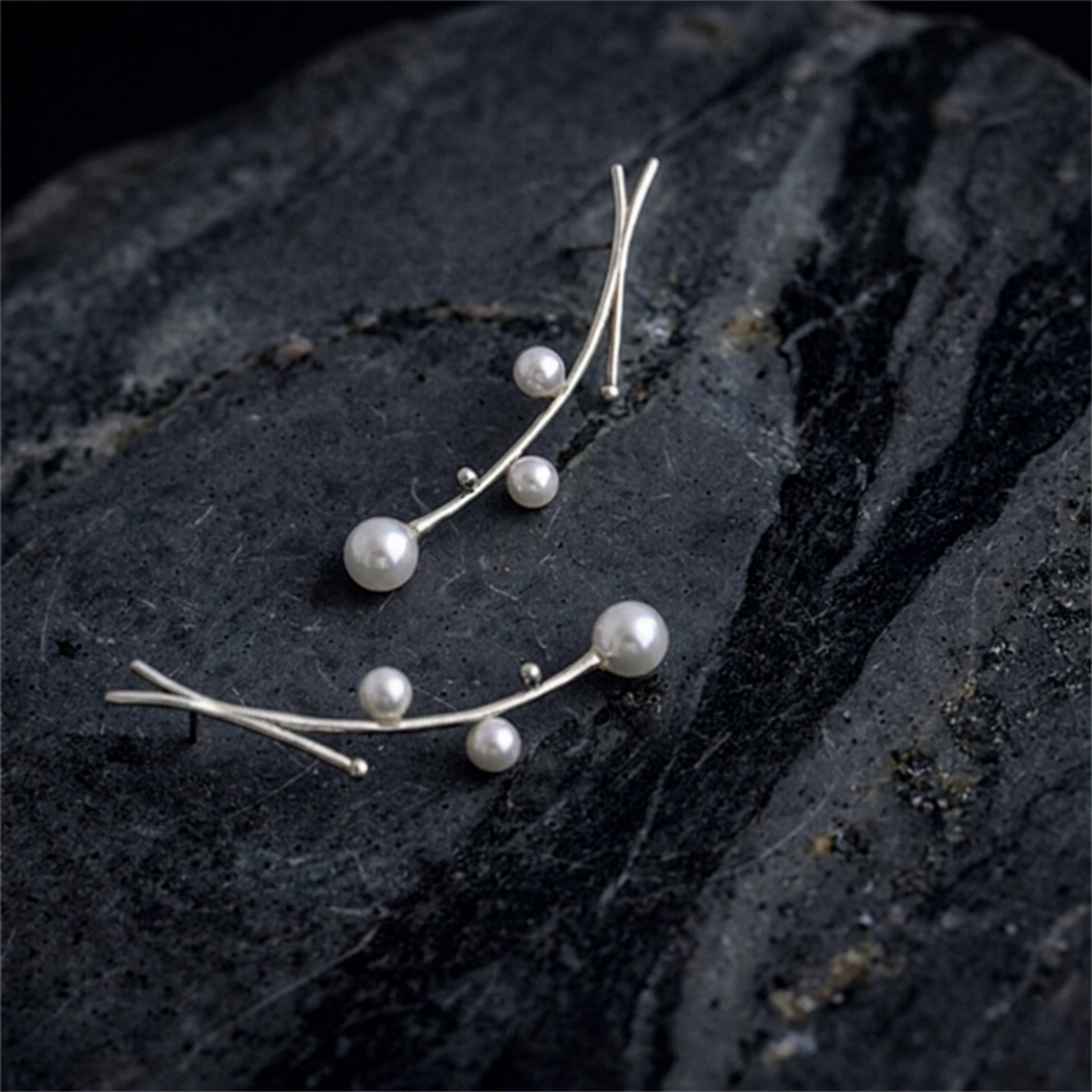 Pearl drop earrings on dark stone, silver wire branches with dangling white pearls