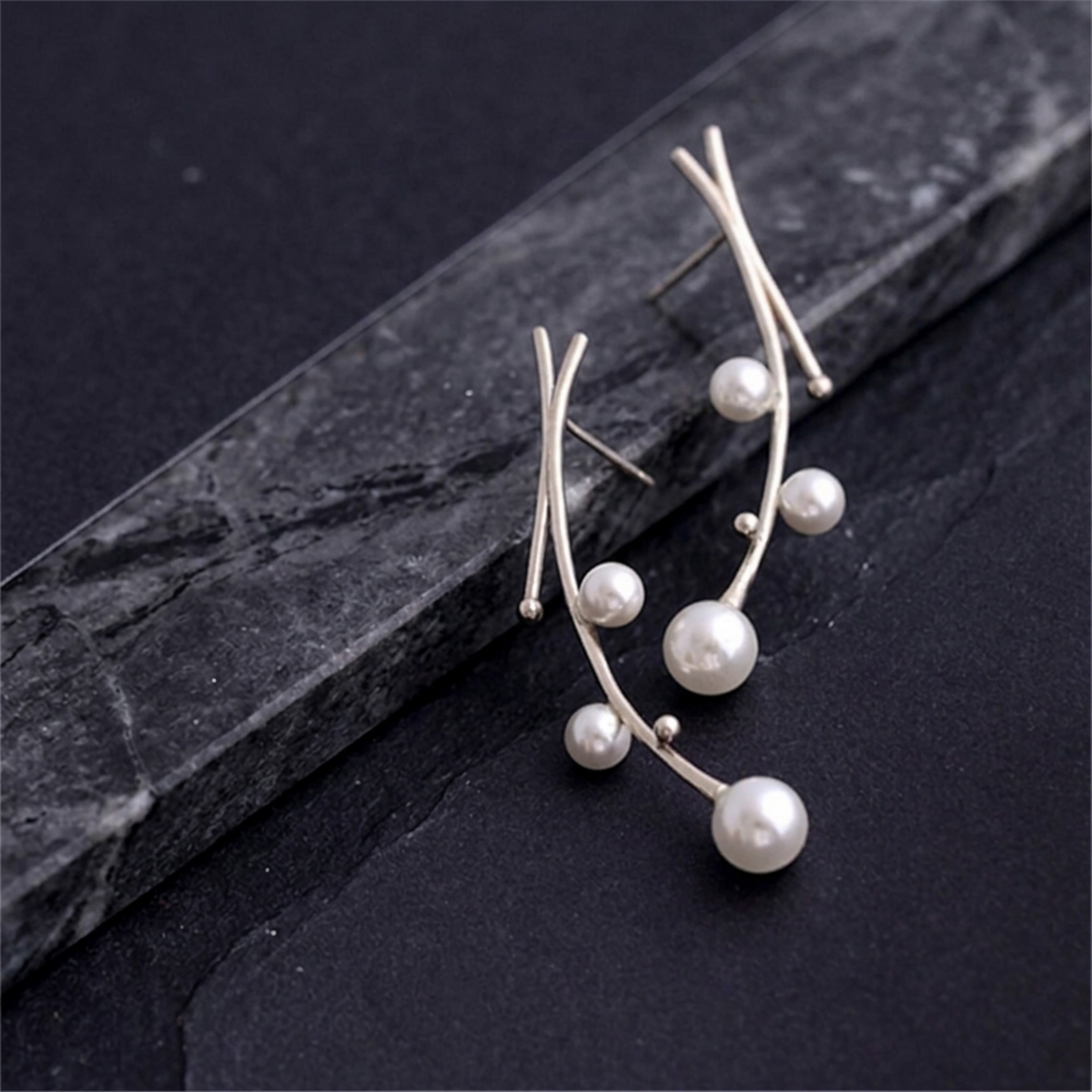 Pearl drop earrings set on dark stone: curved silver wires with multiple white pearls