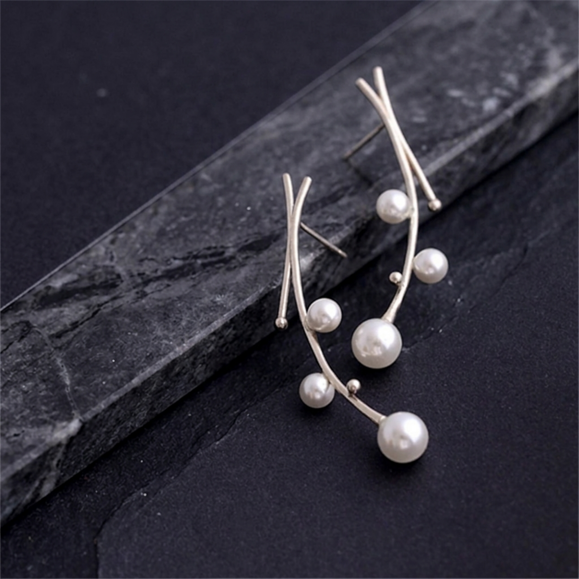Pearl drop earrings set on dark stone: curved silver wires with multiple white pearls