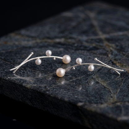 Pearl drop earrings on dark stone, delicate silver arcs with small white pearls