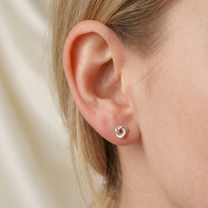 Silver knot stud earrings on ear, small round swirl design