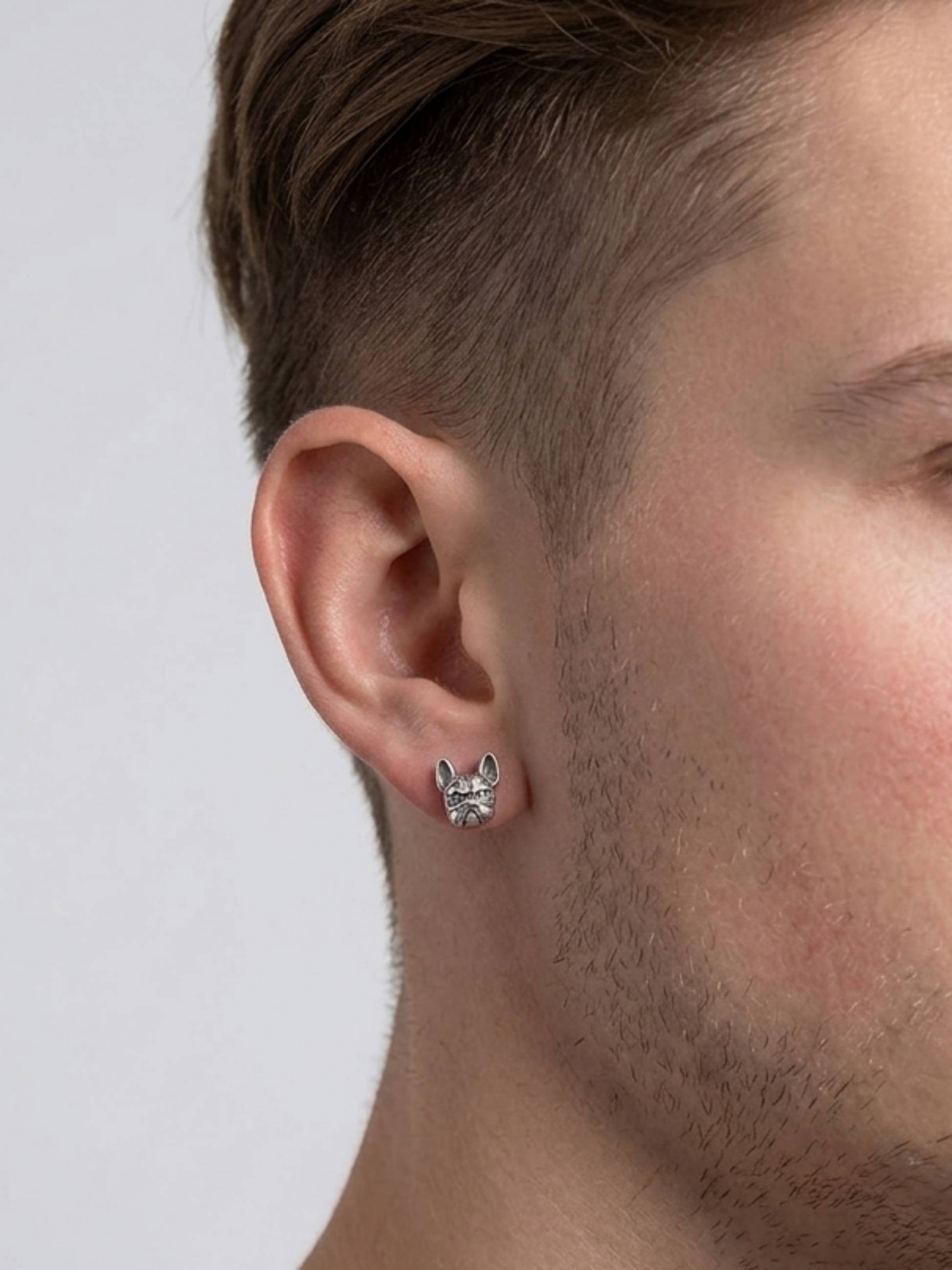 Oxidised bulldog stud earrings on ear, small silver-tone dog face studs