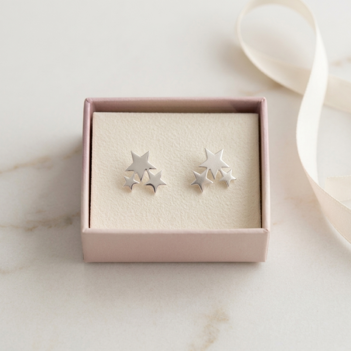 Silver triple star stud earrings in a pink gift box, close-up