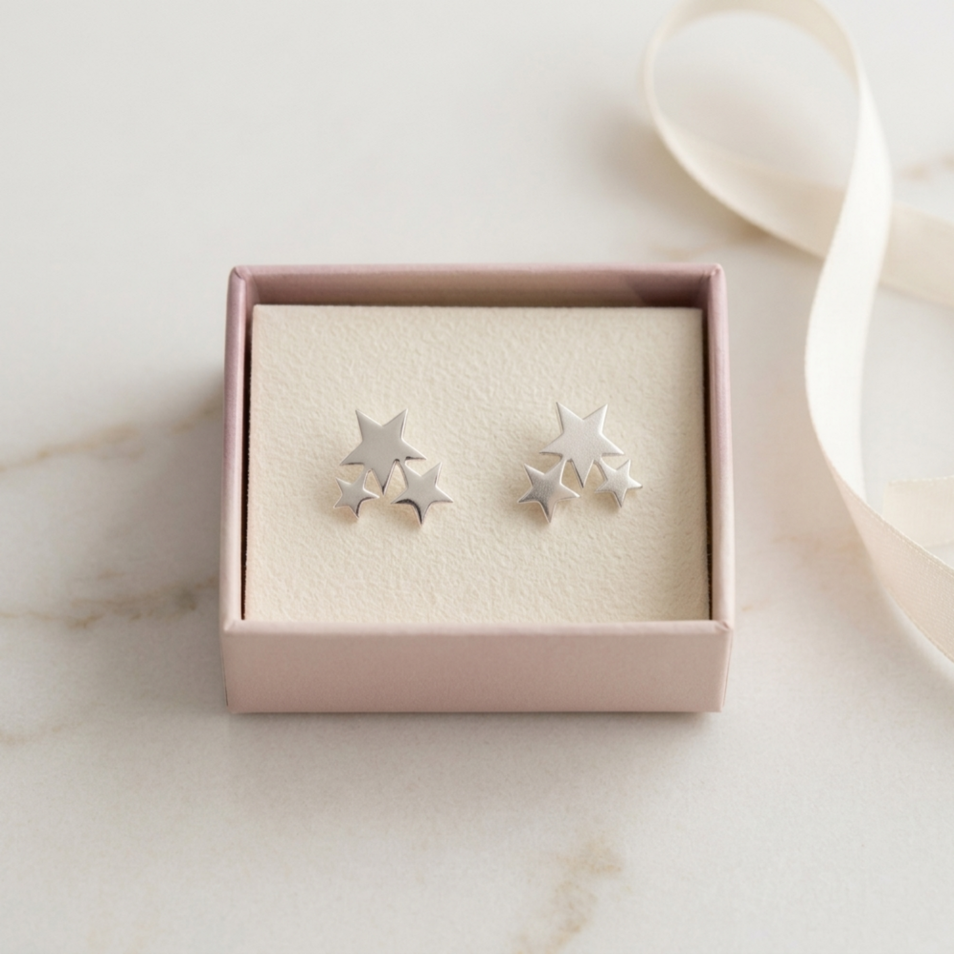 Silver triple star stud earrings in a pink gift box, close-up