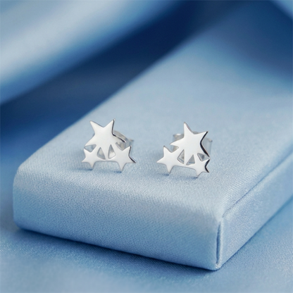 Silver triple star stud earrings on light blue fabric, side view