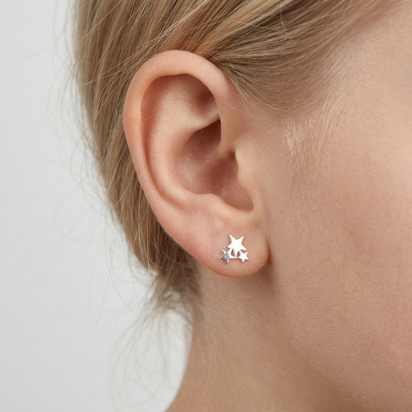 Silver triple star stud earrings on model’s ear, three-star cluster