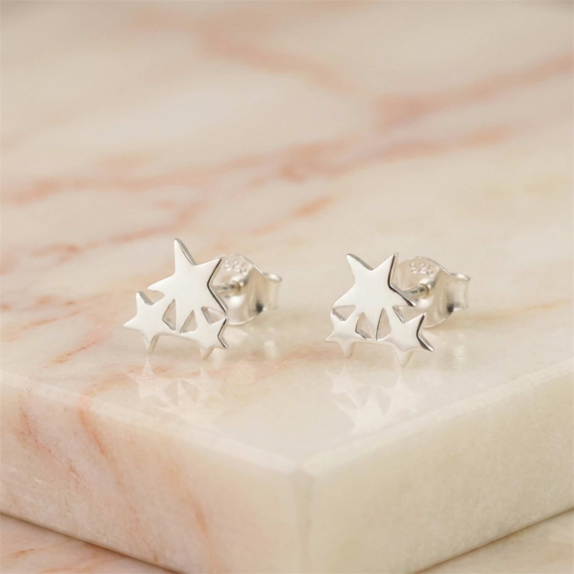 Silver triple star stud earrings on light stone surface, close-up