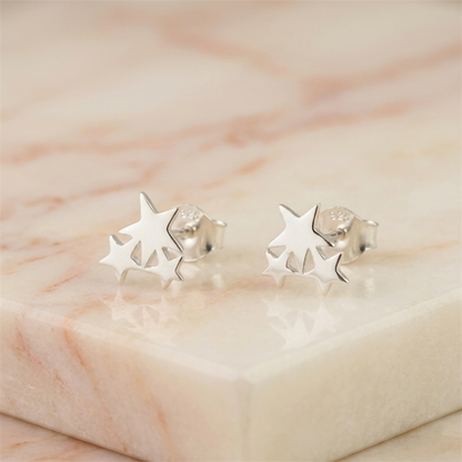 Silver triple star stud earrings on light stone surface, close-up