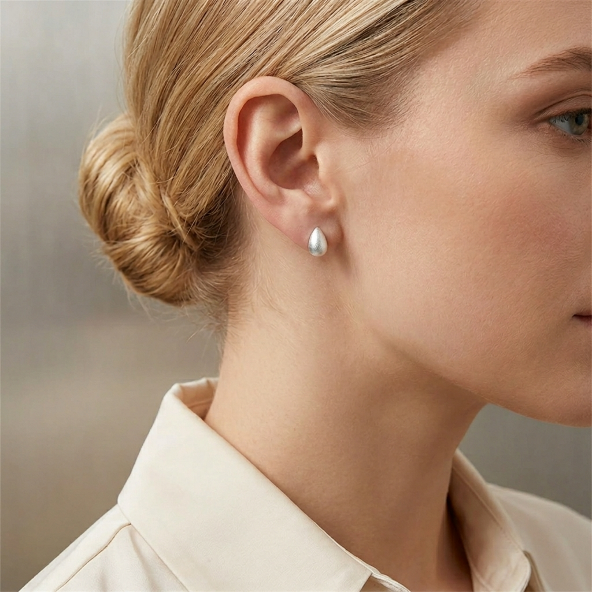 Teardrop stud earrings on ear, silver-toned brushed finish
