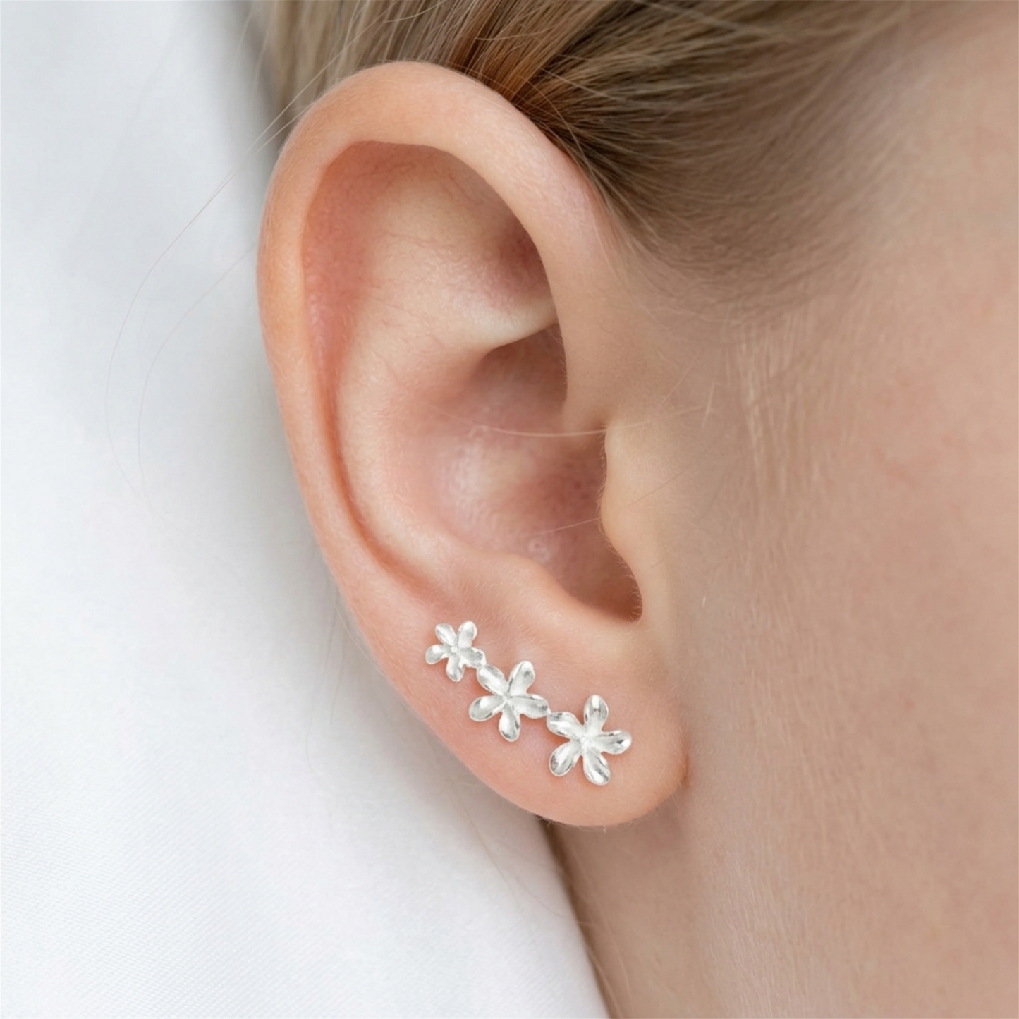 Silver lily flower stud earrings worn on ear, side view
