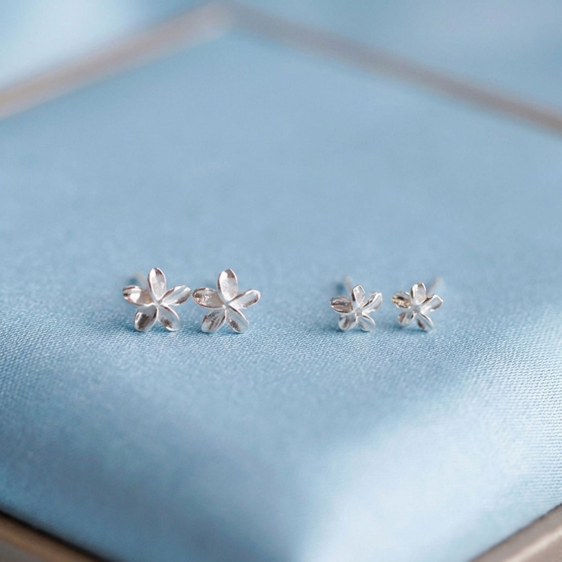 Silver lily flower stud earrings, close-up on blue fabric