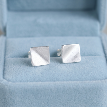 Matte cube stud earrings in brushed silver on visible post backs.