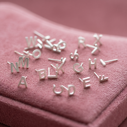 Alphabet letter stud earrings, silver-tone letters displayed on pink velvet