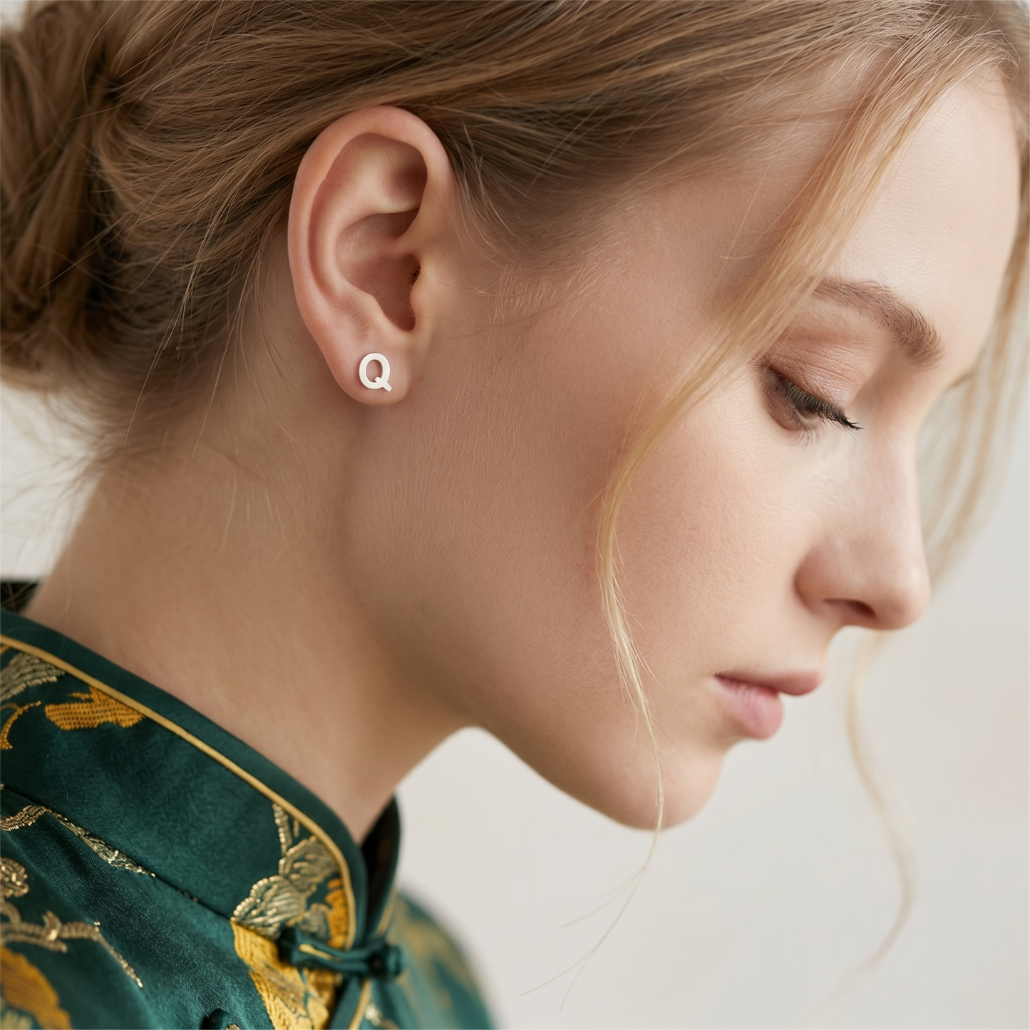 Letter Q stud earrings, silver-tone, on model's ear