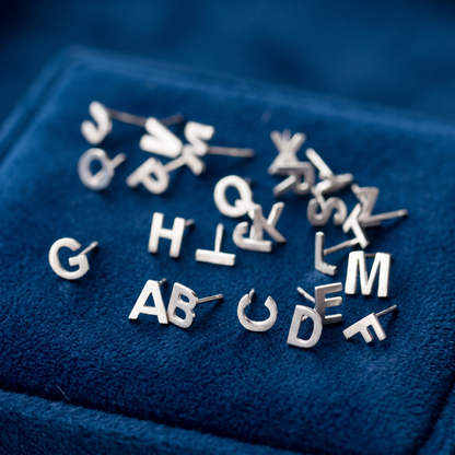 Alphabet letter stud earrings, silver-tone letters displayed on blue velvet