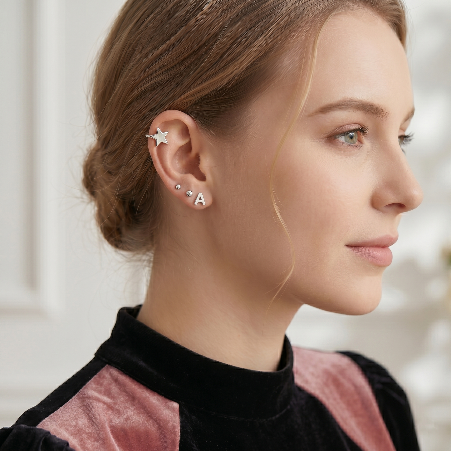 Letter A stud earrings with star-shaped stud, silver-tone, on model's ear