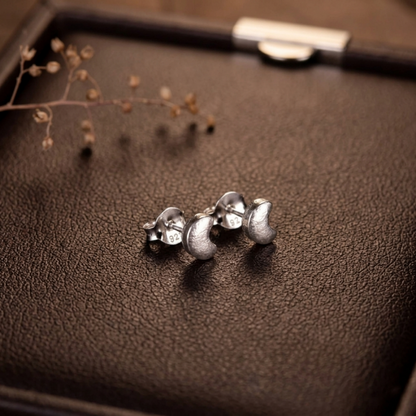 Crescent moon stud earrings, silver-tone, on dark leather