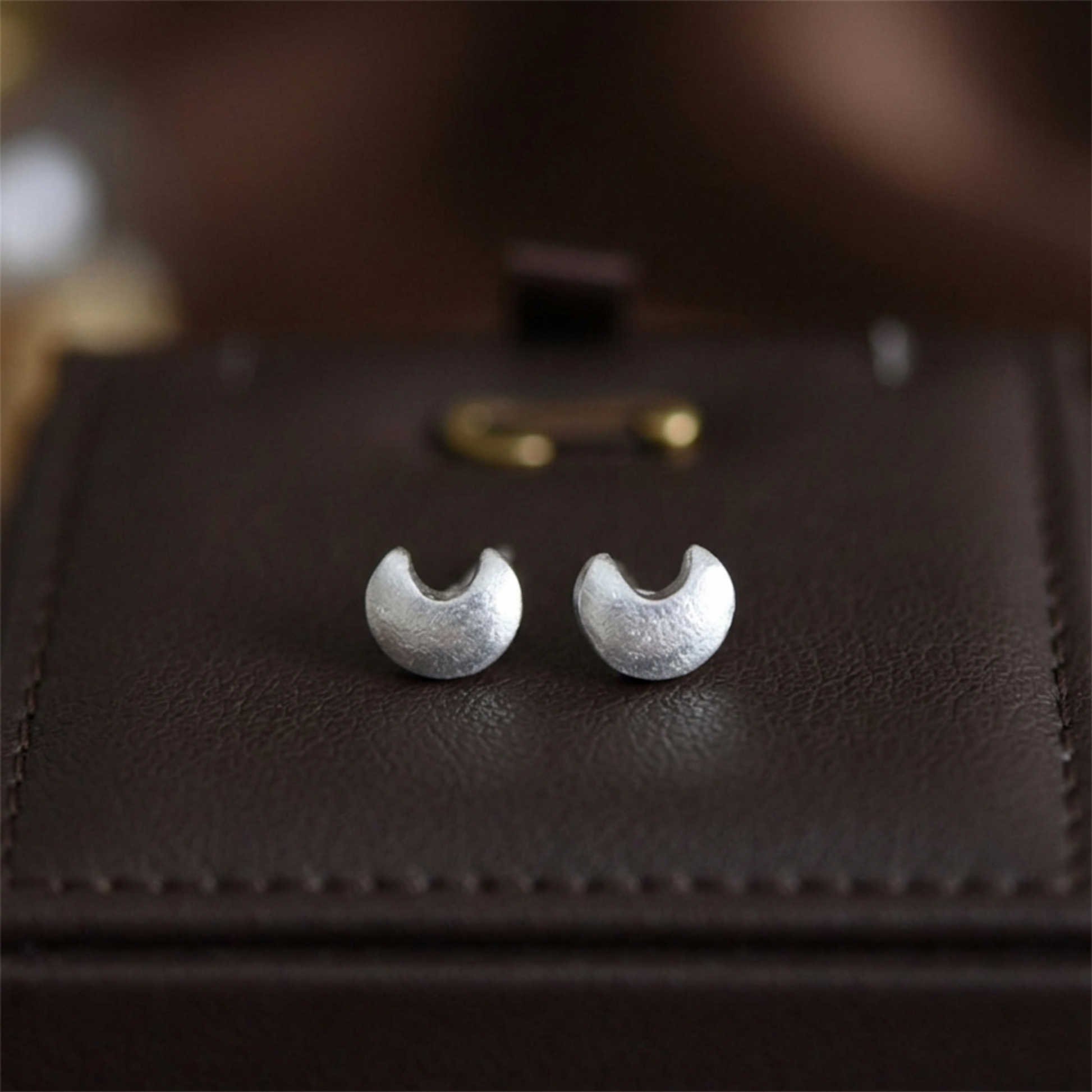 Crescent moon stud earrings, silver-tone, on leather close-up