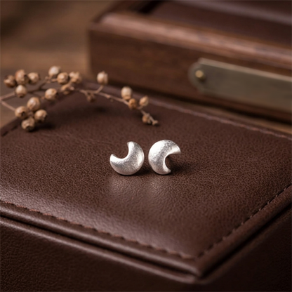 Crescent moon stud earrings, silver-tone, close-up on leather