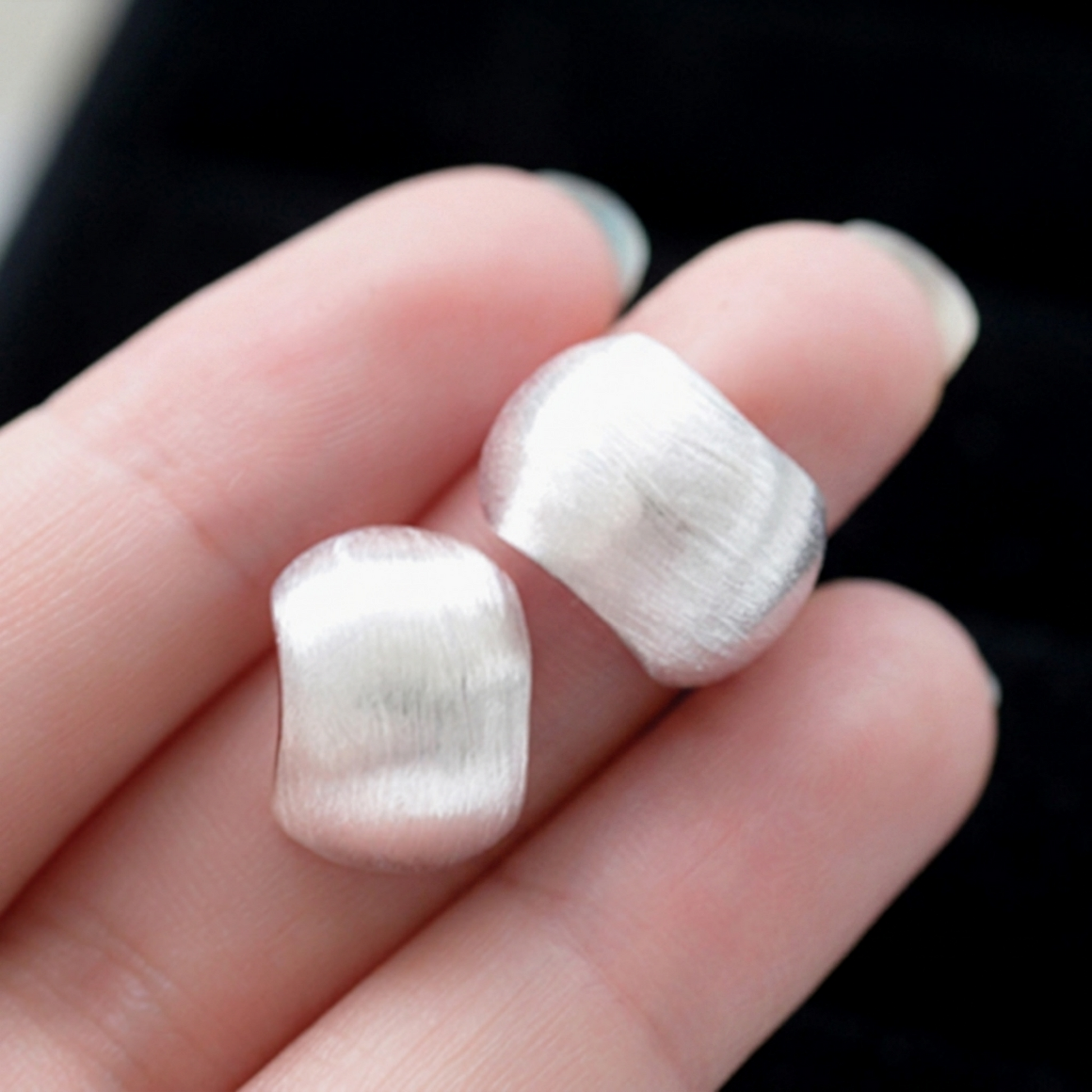 Brushed half-hoop drop earring pair, silver-tone brushed texture close-up on fingers.