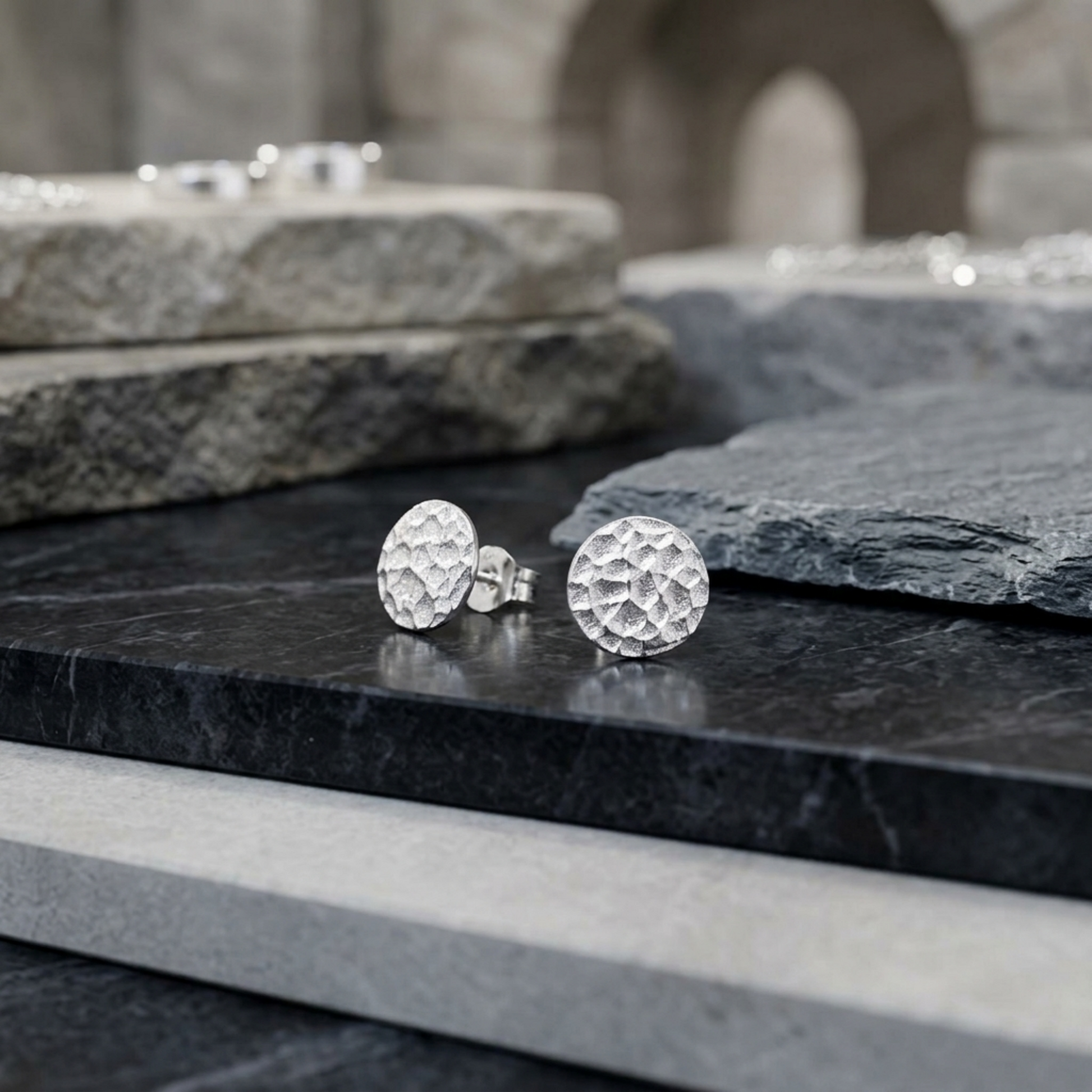Silver hammered disc stud earrings on dark stone surface