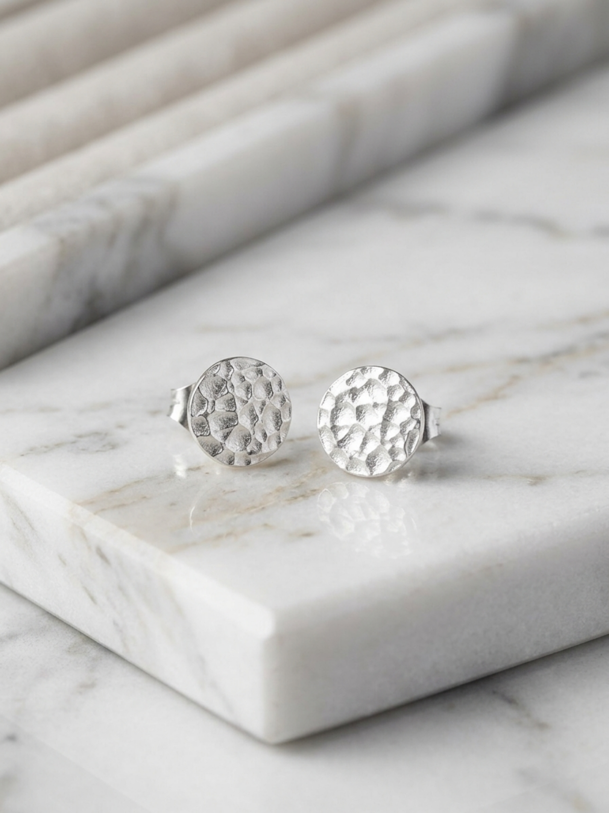Silver hammered disc stud earrings on white marble pedestal