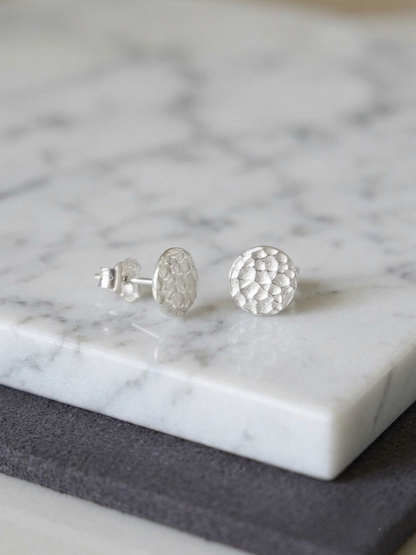 Silver hammered disc stud earrings with round textured discs on white marble