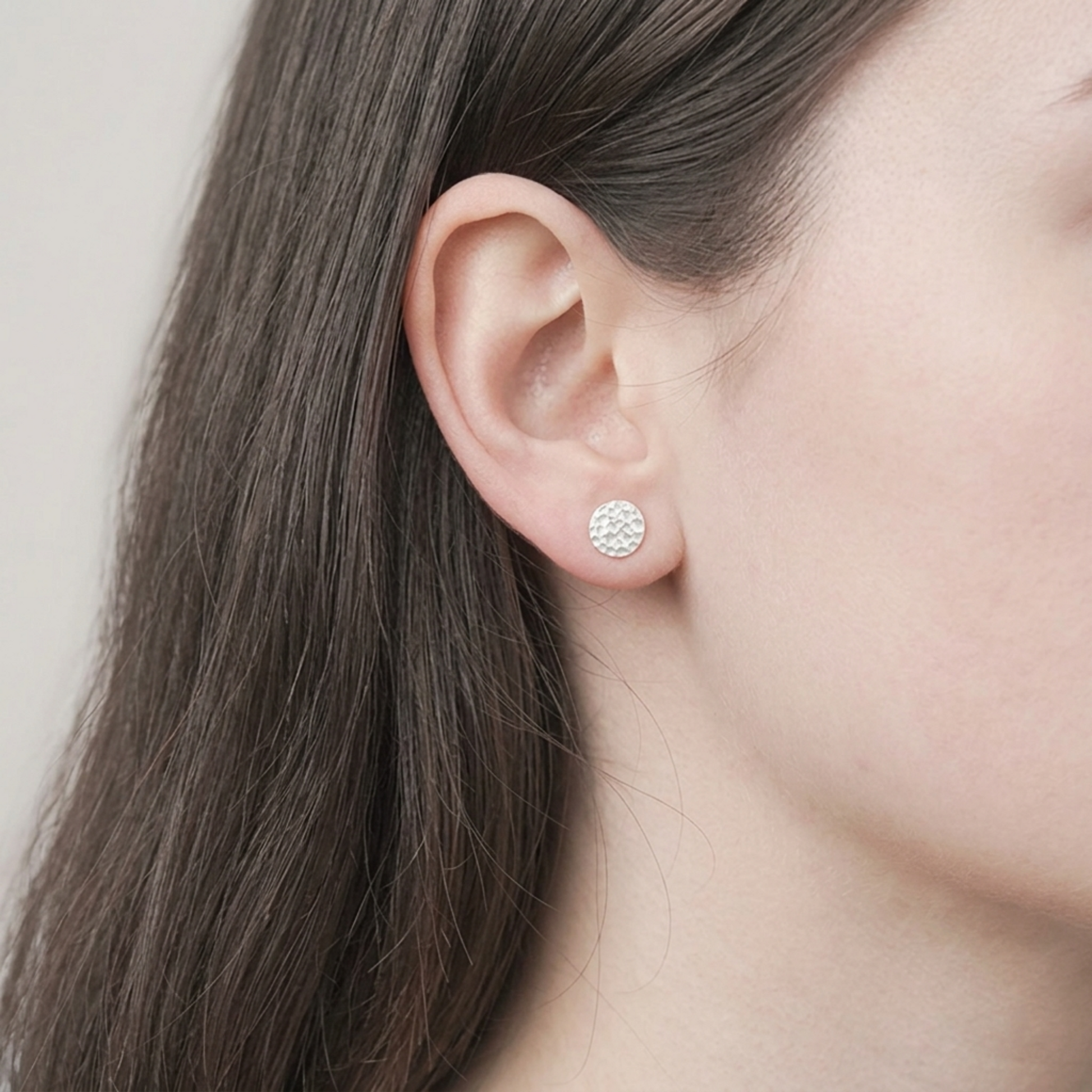 Silver hammered disc stud earring on ear with round textured face