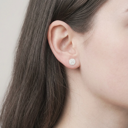 Silver hammered disc stud earring on ear with round textured face