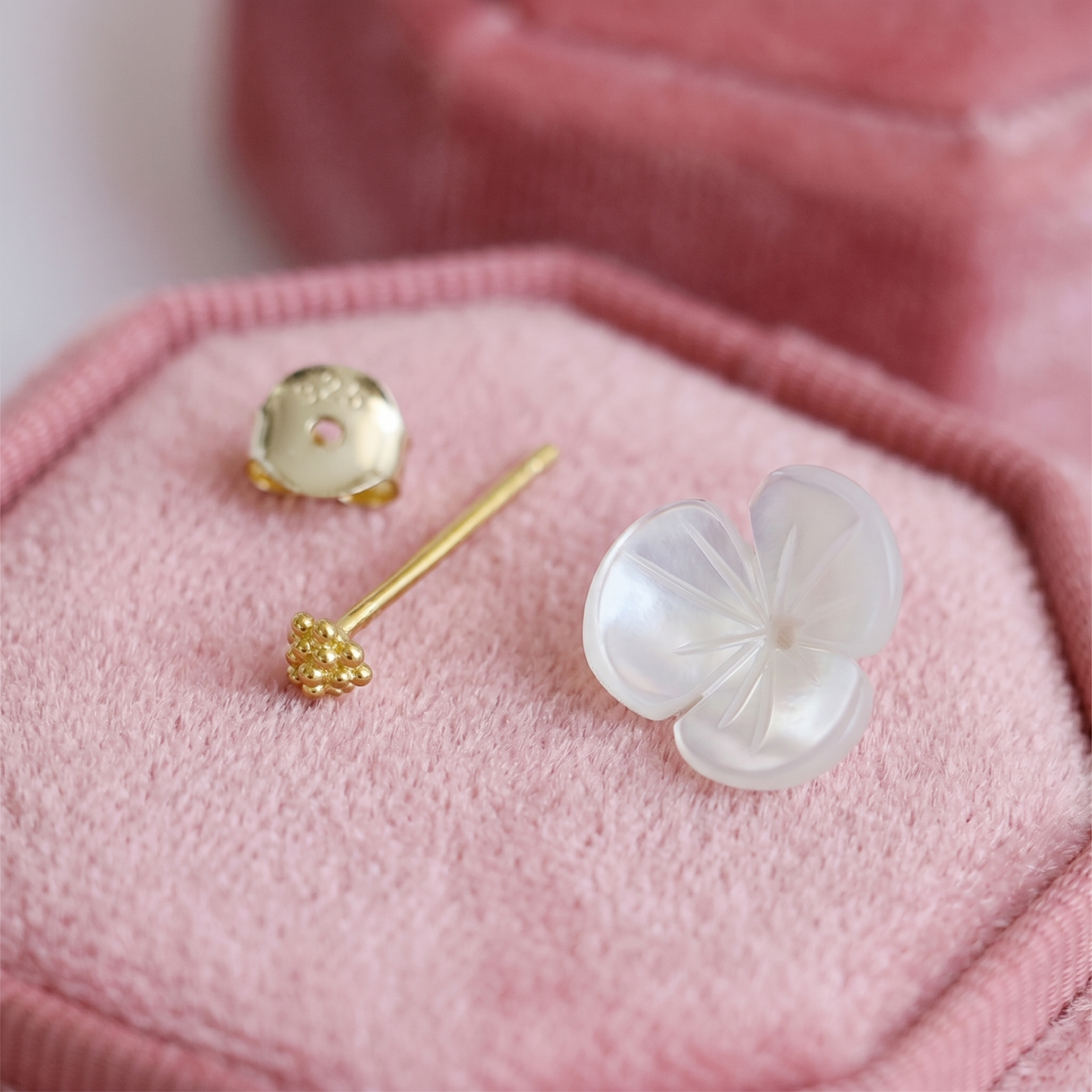 White flower stud earrings with gold-tone backs and posts on pink fabric