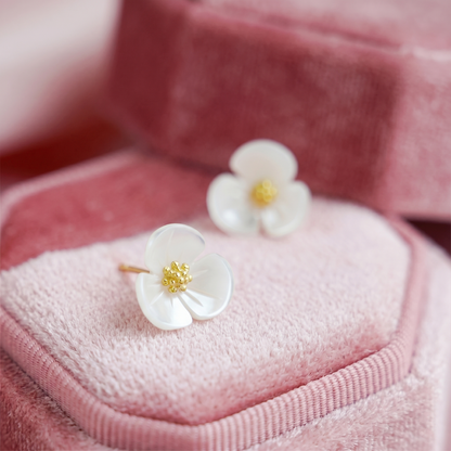 White flower stud earrings with gold-tone centers on pink velvet cushion