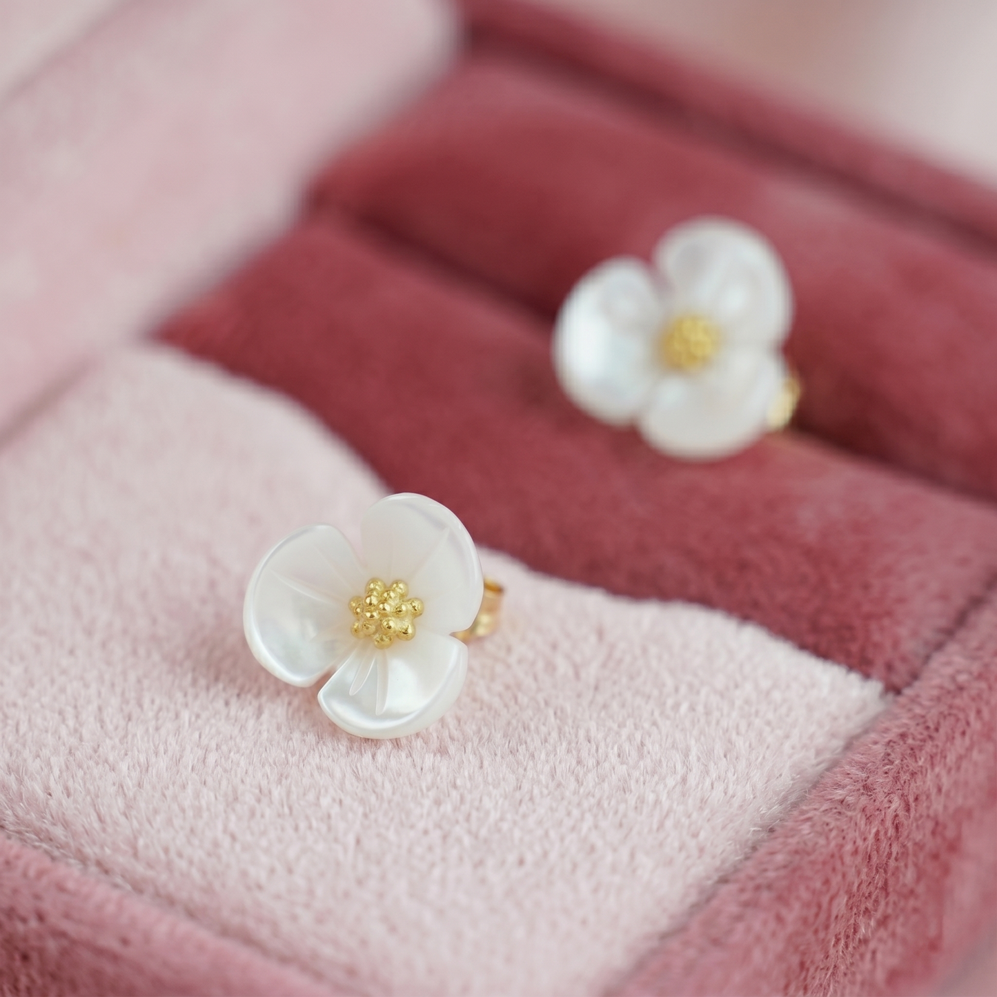 White flower stud earrings with gold-tone center on pink fabric display